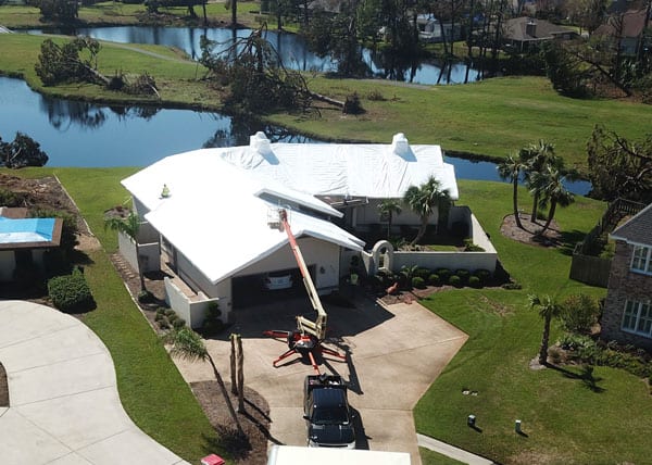 Storm-damaged home sealed with white shrink wrap